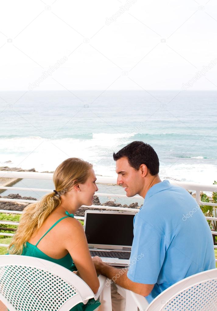 Happy young couple using laptop on balcony