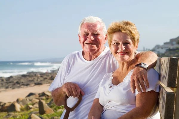 Happy senior couple sitting on beach bench — Stock Photo, Image