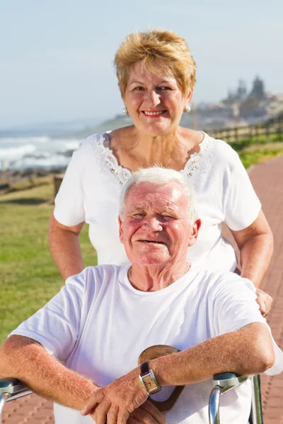 Senior man being pushed on wheelchair by his wife — Stock Photo, Image