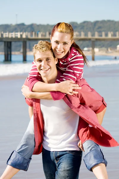Счастливая молодая пара играет на пляже — стоковое фото