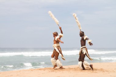 Two african zulu men dancing on beach clipart