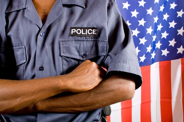 Afrikanischer amerikanischer Polizist steht vor US-Flagge — Stockfoto