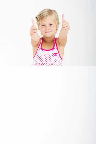 Happy little girl giving thumbs up behind white board — Stock Photo, Image