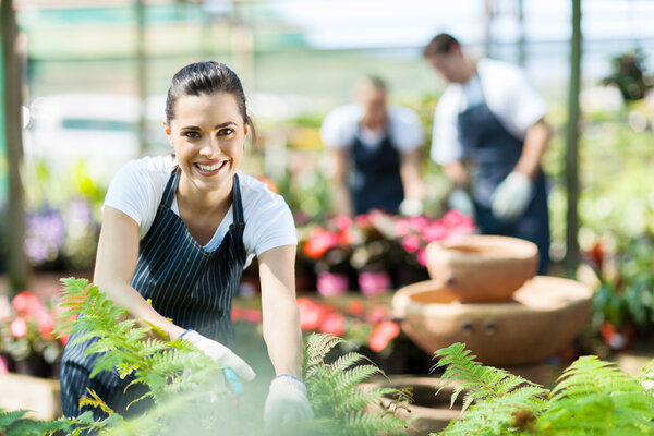 Happy female nursery worker trimming plants in greenhouse