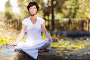 Middle aged woman doing yoga meditation outdoors clipart