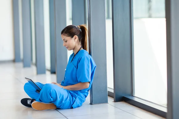 Hübsche Krankenschwester sitzt auf dem Boden und benutzt in der Pause einen Laptop — Stockfoto