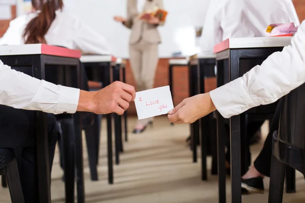 Menino da escola passando um Eu amo Você nota para uma menina na sala de aula — Fotografia de Stock