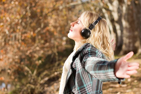 Молода жінка слухає музику в осінньому лісі — стокове фото