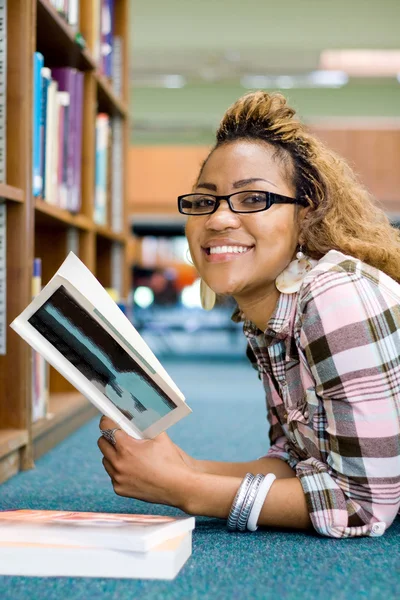 Chica universitaria afroamericana feliz leyendo libro en la biblioteca — Foto de Stock