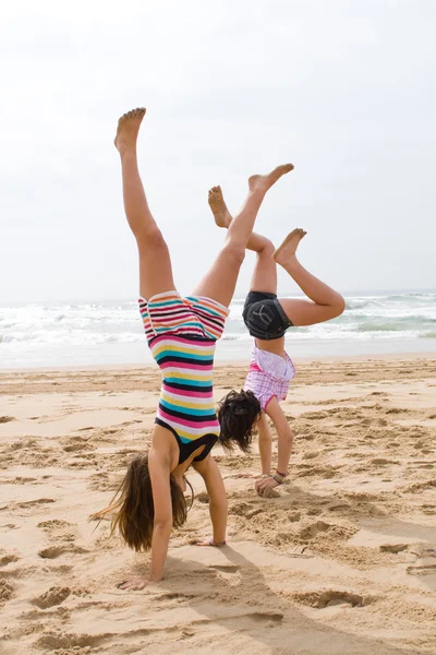 Twee tiener meisjes doen handstand op strand — Stockfoto