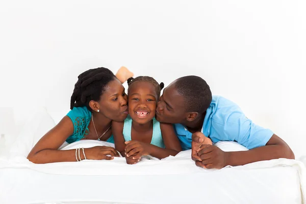 Ευτυχής αφροαμερικάνων γονείς φιλιά κόρη στο κρεβάτι — Φωτογραφία Αρχείου