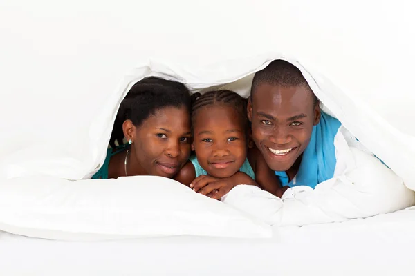 Gelukkige Afro-Amerikaanse familie onder dekbed op bed ligt — Stockfoto