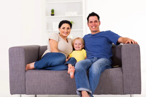 Jovem família feliz sentado no sofá em casa — Fotografia de Stock