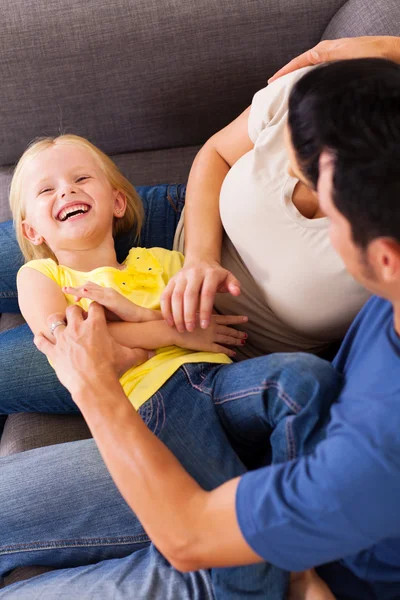 Pais cócegas pequena filha no sofá — Fotografia de Stock