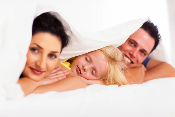 Schattig klein meisje dutten met ouders op bed — Stockfoto