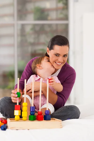 Cute daughter kissing mother while playing with toy — Stock Photo, Image