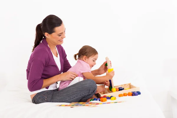 Liten flicka spela pedagogiska leksak med mamma på sängen — Stockfoto