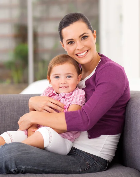 Ganska mamma kramar söta lilla dotter på soffa — Stockfoto
