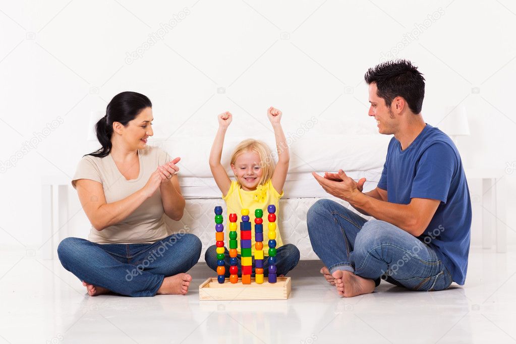 Happy little girl playing toys with parents on bedroom floor