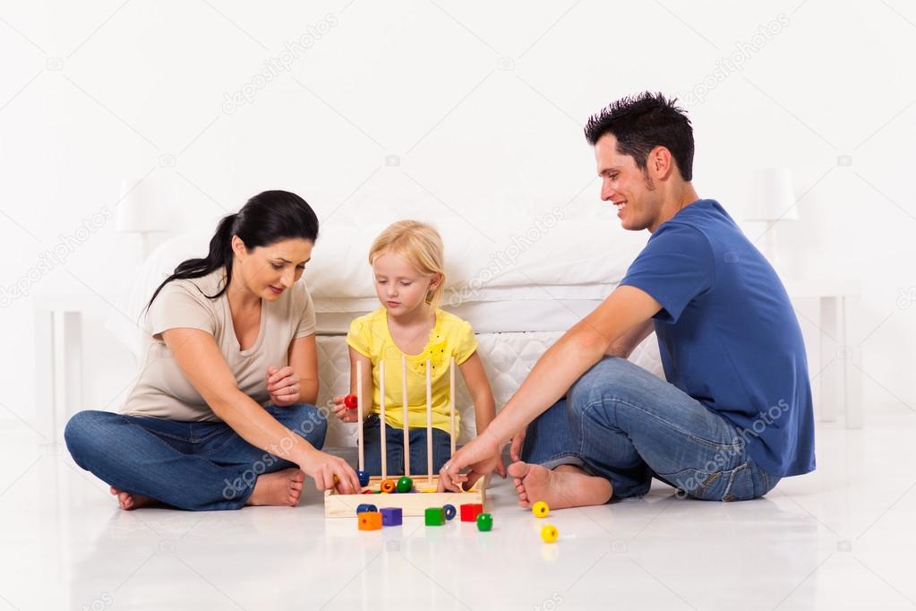 Happy family playing toy game with daughter on bedroom floor