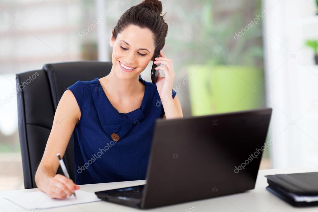 Cute young office worker talking on cell phone in office