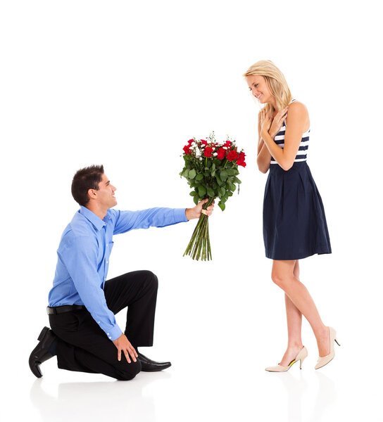 Young man down on his knee to give bunch of roses to a woman
