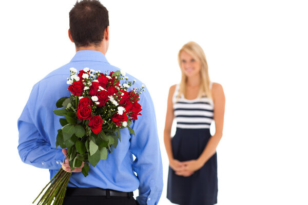 Young man hiding bunch of roses behind his back to surprise his girlfriend on valentine's day
