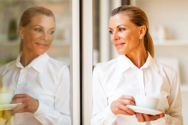 Elegante empresária sênior olhando fora do escritório com café — Fotografia de Stock