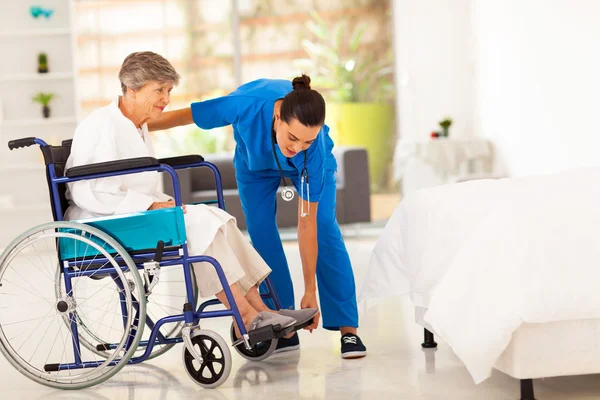 Young caregiver helping elderly woman on wheelchair — Stock Photo, Image