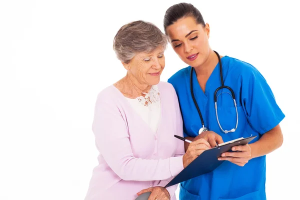 Senior vrouw ondertekening medisch formulier met hulp van verpleegster — Stockfoto