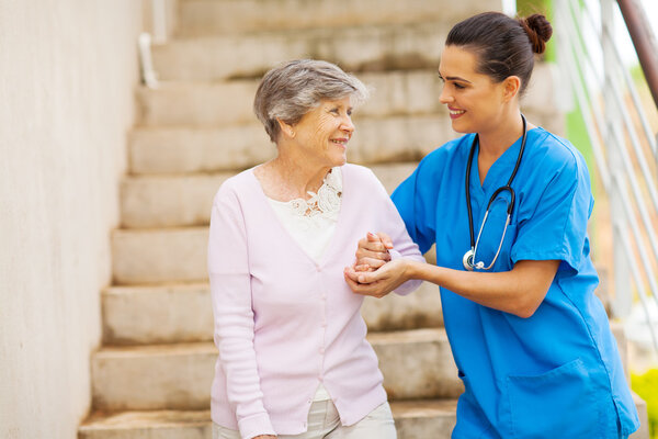 Young caregiver helping senior woman walking down stairs
