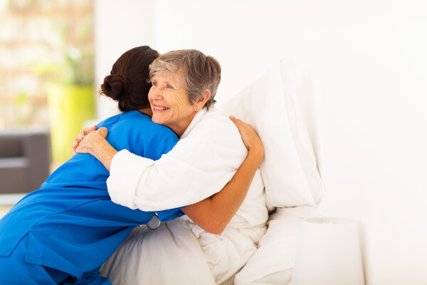 Happy elderly woman hugging caregiver on bed