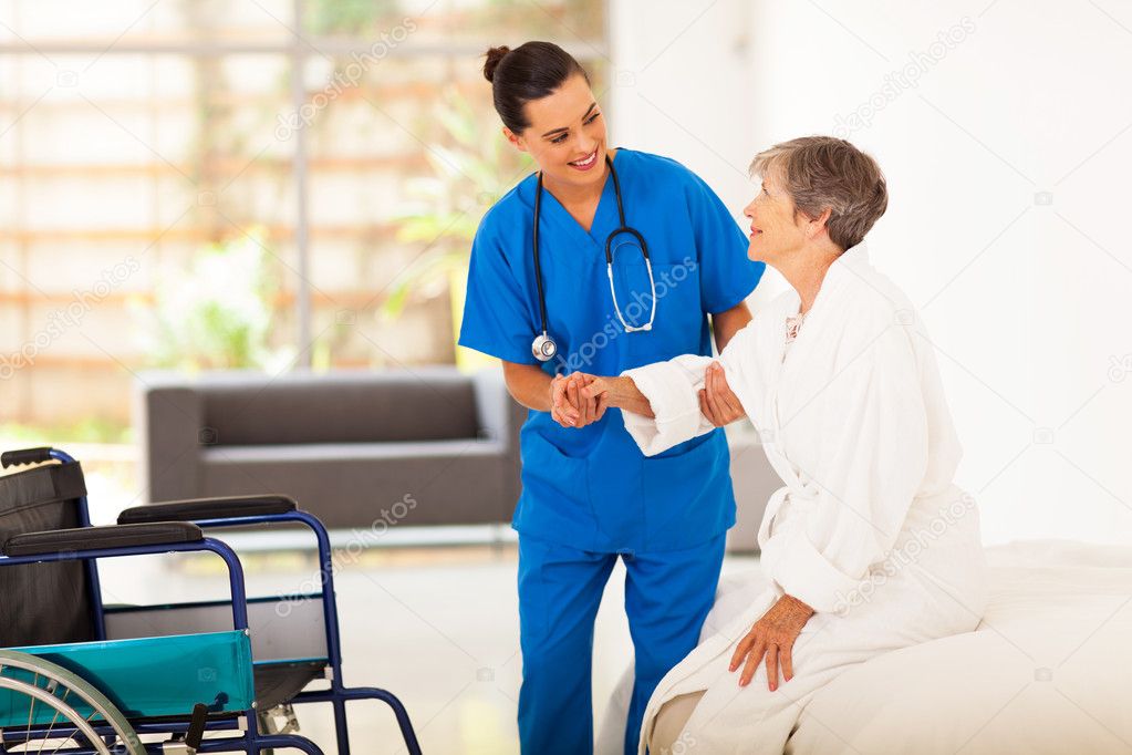 Young female caregiver helping senior woman getting up