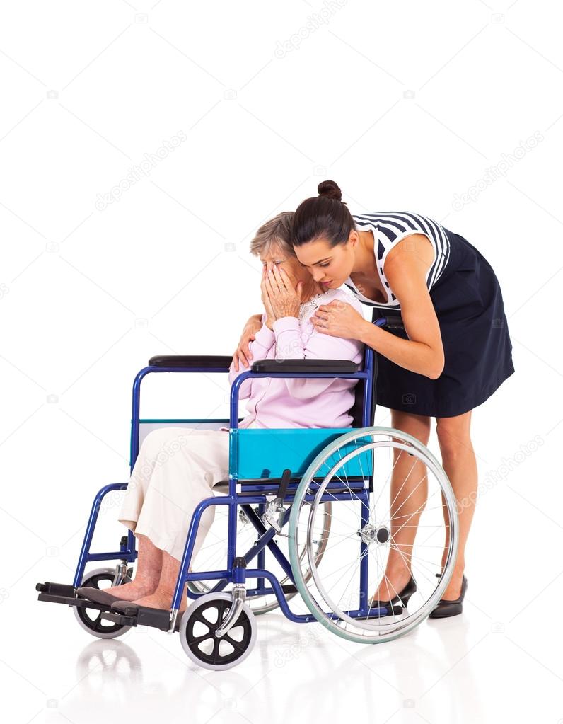 Young female caregiver hugging and comforting lonely disabled senior woman