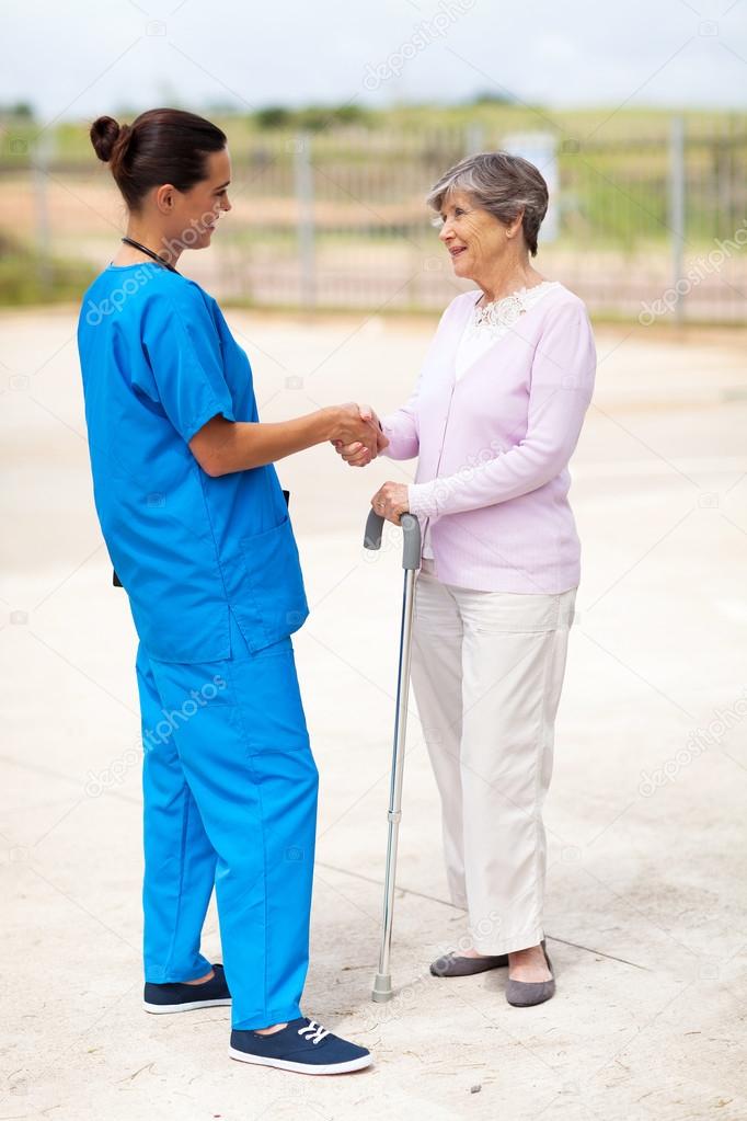 Young nurse in uniform talking to senior woman outdoors
