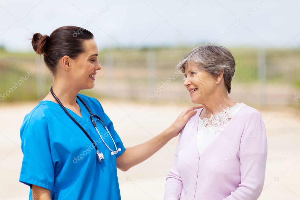 Happy young nurse talking to senior woman outdoors