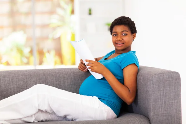 Schwangere Afroamerikanerin liest zu Hause auf dem Sofa — Stockfoto
