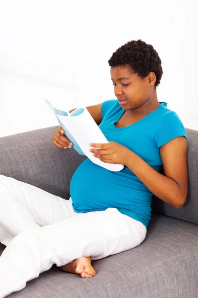 Mujer africana embarazada leyendo en sofá —  Fotos de Stock