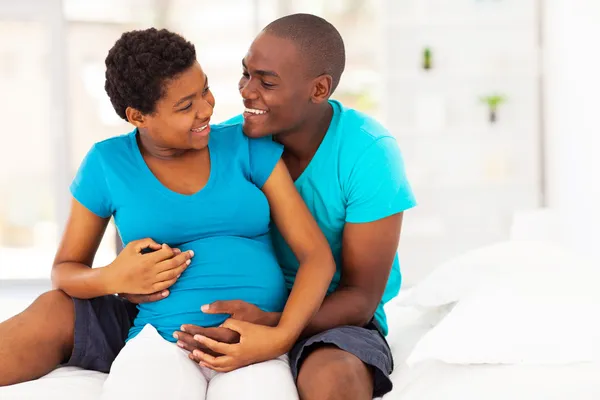 Feliz mulher grávida afro-americana e marido abraçando na cama — Fotografia de Stock