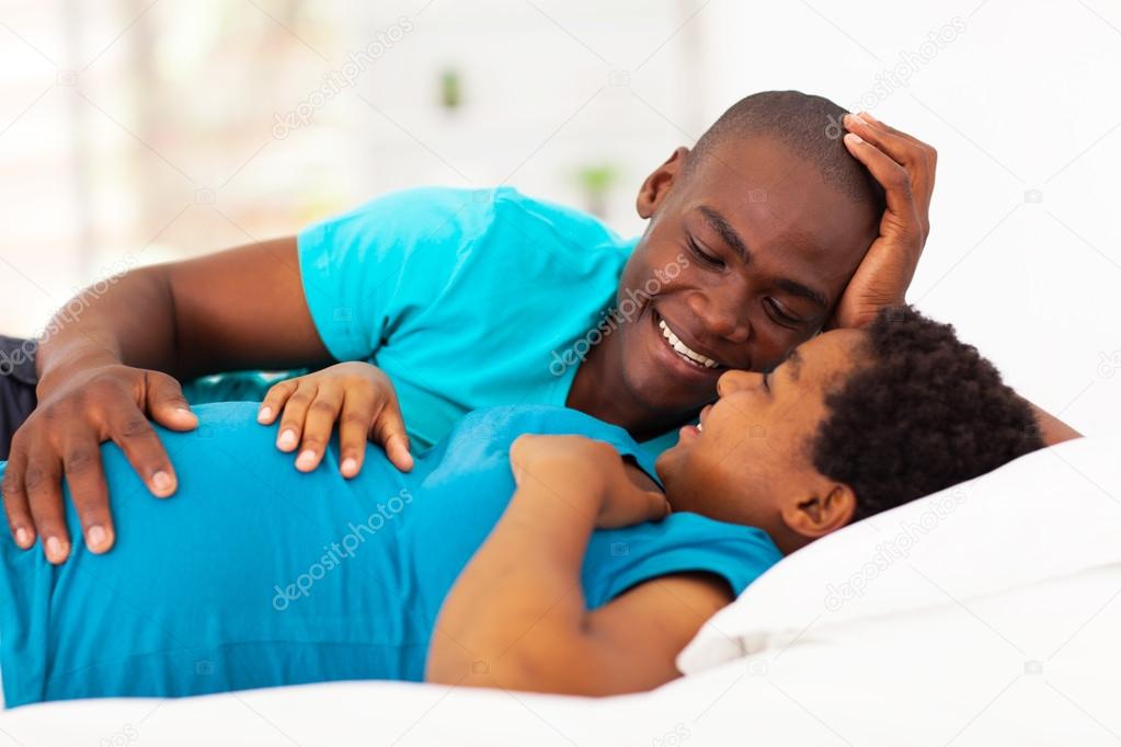 expecting african american couple lying on bed and chatting