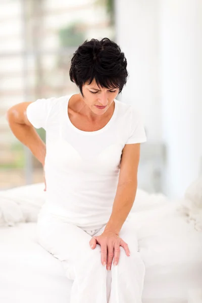 Женщина, сидящая на кровати с болью в спине — стоковое фото