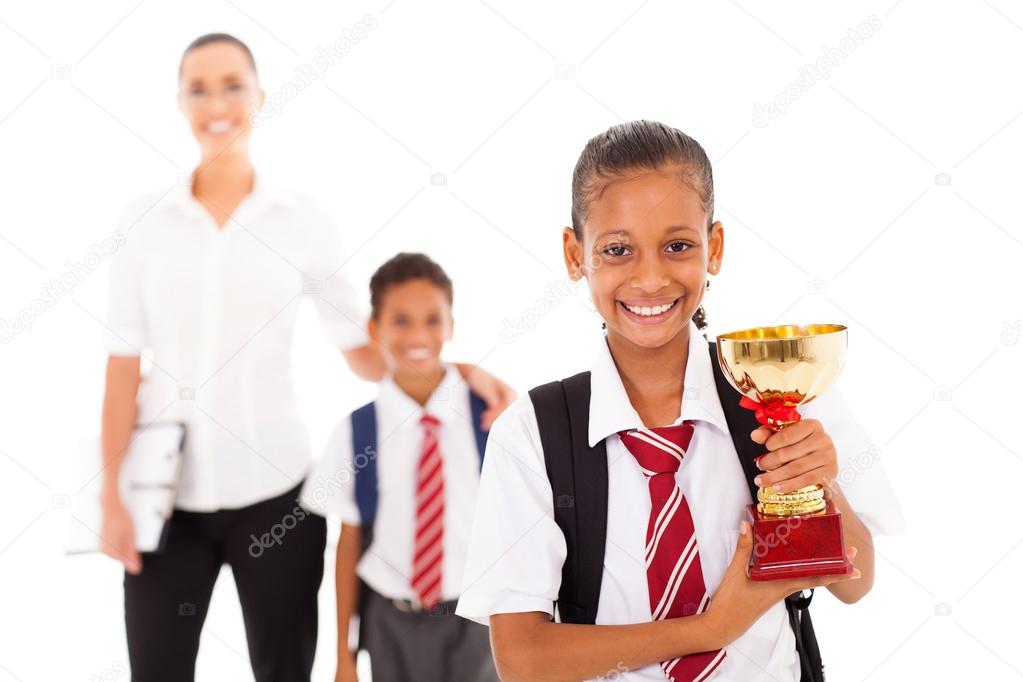 Schoolgirl holding trophy in front of teacher and classmate