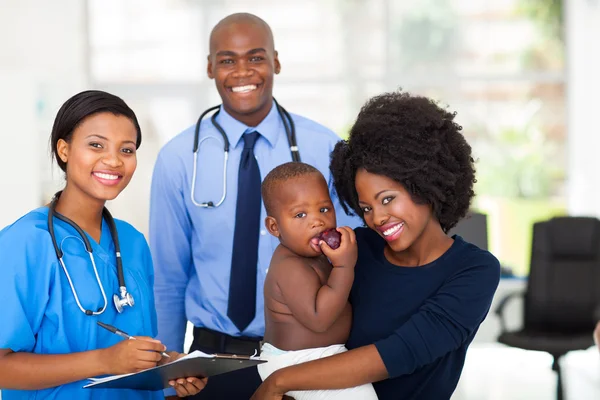 Mãe segurando seu bebê após check-up com enfermeira e médico — Fotografia de Stock