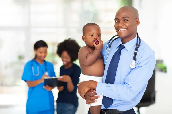 Мужчина врач держа ребенка с матерью и медсестрой на заднем плане — стоковое фото