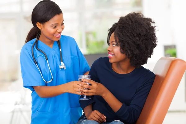 Freundliche afrikanische Krankenschwester gibt geduldigem Wasser — Stockfoto