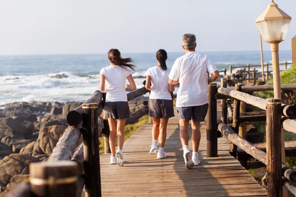 Bakifrån av familjen jogging på stranden — Stockfoto