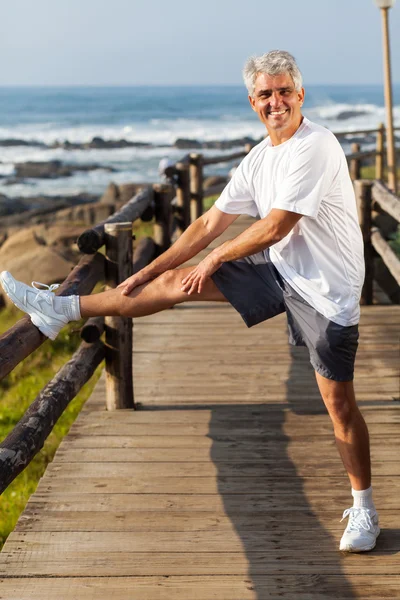 Aktive ältere Mann streckt Bein am Strand — Stockfoto