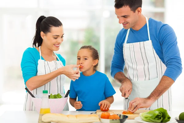 Klein meisje proeverij tomaat terwijl ouders koken — Stockfoto