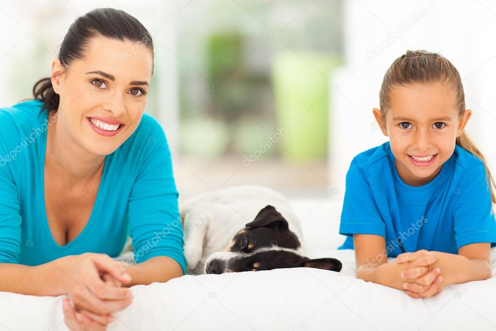 mother daughter and pet dog lying on bed