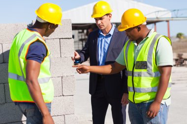 construction workers with their manager checking bricks clipart
